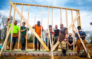 People stand in the midst of a framed wall on a new construction site.