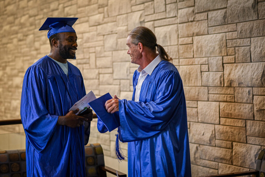 Two older men in graduation gowns talk in the lobby.