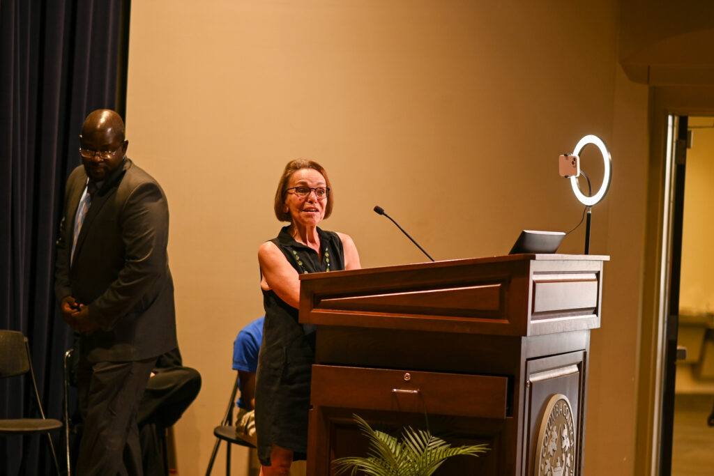 An older woman smiles, standing behind the podium