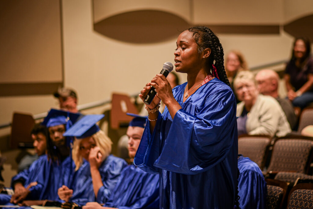 A woman speaks into a microphone, tears running down her cheeks.