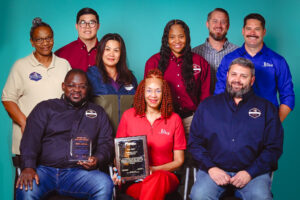 A group of people stand together holding two award plaques.